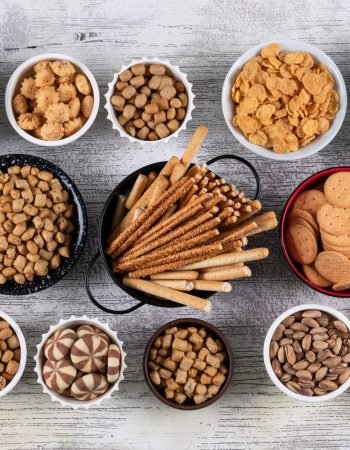 top-view-different-kind-snacks-as-nuts-crackers-cookies-bowls-white-wooden-surface-horizontal