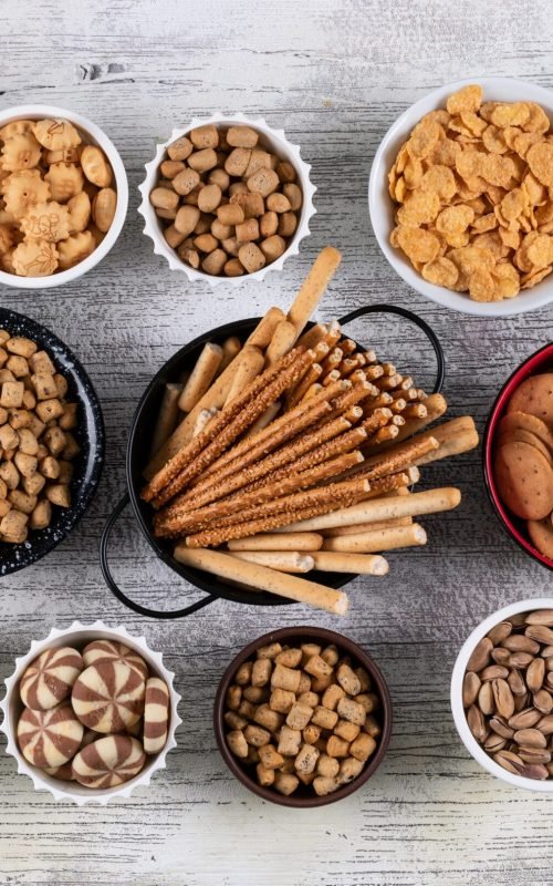 top-view-different-kind-snacks-as-nuts-crackers-cookies-bowls-white-wooden-surface-horizontal
